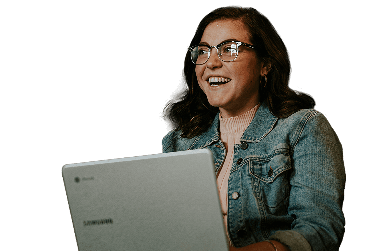 Mujer joven con gafas y chaqueta de mezclilla sonriendo mientras usa una laptop